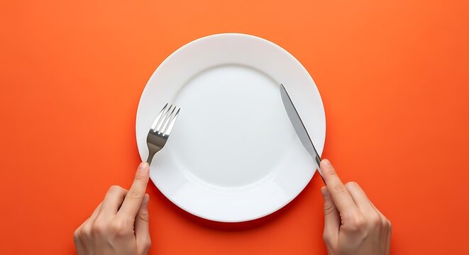 Empty white plate with cutlery on bright orange background overhead shot