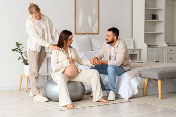 Young pregnant woman sitting on fitness ball with her husband and doula in bedroom