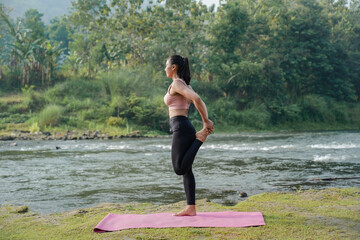 A slender Asian girl with brown skin in sportswear is doing stretching movements of her quadriceps...