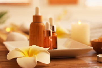 Tray with bottles of cosmetic products and plumeria flower on table in interior of spa salon, closeup