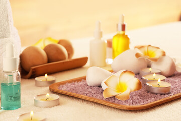 Tray, sea salt, plumeria flowers and burning candles on white couch in spa salon, closeup