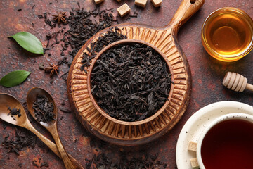 Cup of hot black tea with dry leaves and glass bowl of honey on dark background