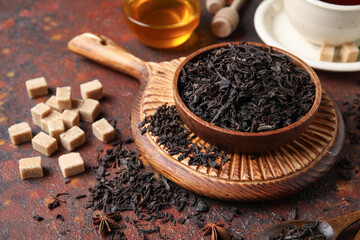 Bowl with dry black tea leaves and cubes of sugar on dark background