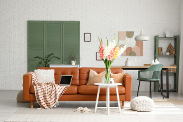 Folding screen, comfortable sofa, table and vase with gladiolus flowers in interior of living room