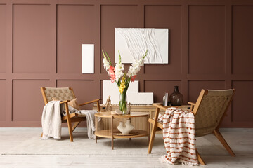 Wicker armchairs, table and vase with gladiolus flowers in interior of living room