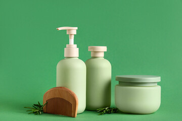 Composition with wooden hair comb, rosemary twigs, jar and bottles of cosmetic products on green background, closeup