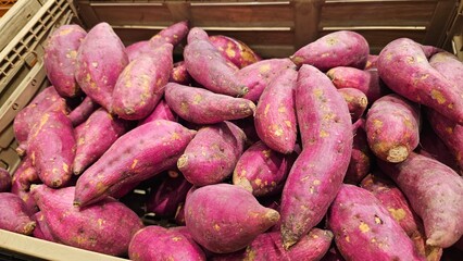 Fresh purple sweet potatoes piled high in a market bin, showcasing vibrant color and natural texture, ready for culinary use.