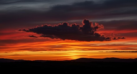 Dramatic sunset with vibrant orange and red hues over silhouette landscape and clouds