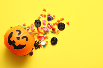 Overturned cauldron in shape of pumpkin with different candies for Halloween on yellow background