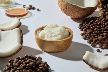 Still life with coconuts, coffee beans, and bowl of creamy shea butter arranged on white surface. Designed for spa, skincare, and natural product promotion.