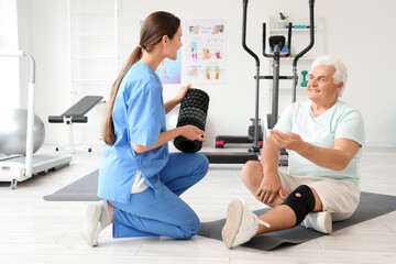 Female therapist with foam roller and senior man in rehabilitation center