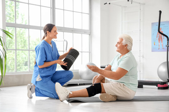 Female therapist with foam roller and senior man in rehabilitation center - Powered by Adobe
