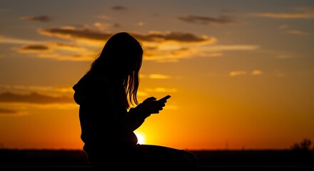 Silhouette of a person using a smartphone during sunset against the horizon