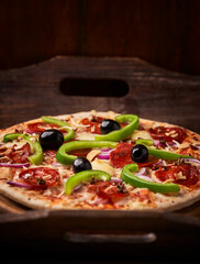 Pizza with chorizo ​​sausage, mozzarella cheese, green pepper and black olives. Rustic wooden background. Soft focus.	