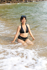 A young Asian woman is happily playing in the sea amidst the waves, smiling brightly.