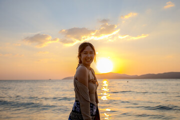 A happy Asian woman is enjoying the nature, sea view, ocean waves, sunset, and a bright smile.