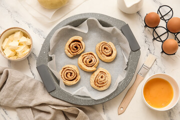 Baking tray with raw cinnamon buns and ingredients on marble background
