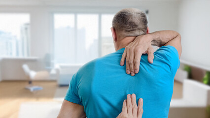 Back view of man feeling muscular pain from his neck to waist. Middle aged man with back pain possibly myofascial release syndrome indoors