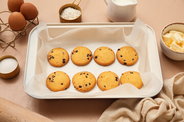 Baking tray with tasty cookies and ingredients on beige background