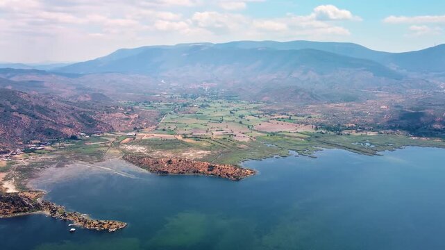 aerial perspective showcasing the serene beauty of Bafa Lake in Turkey. This footage captures the expansive blue waters, the surrounding lush landscapes, and the distant mountains under a clear sky, h
