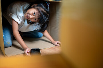 Curious Girl in Cardboard Box: A little girl in a cardboard box, looking at a smartphone and filled with curiosity. She has a mix of wonder, a glimpse into a world of imagination. 