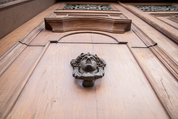 Cinematic close-up of an antique wooden door seen from below, featuring a forged iron handle shaped as a female face with flowing hair, captured in Puebla, Mexico.