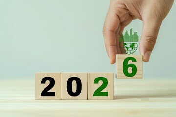 Hand changes wooden block from 2025 to 2026 with green leaf symbol for eco-friendly future concept