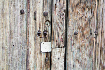 Textured close-up of a rustic, aged wooden door with metal rivets and an antique lock, capturing the simple beauty of worn materials.