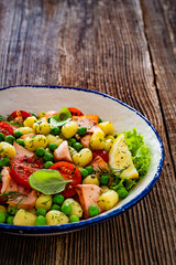 Gnocchi with salmon bites, green peas and cherry tomatoes on wooden table	