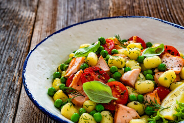 Gnocchi with salmon bites, green peas and cherry tomatoes on wooden table	