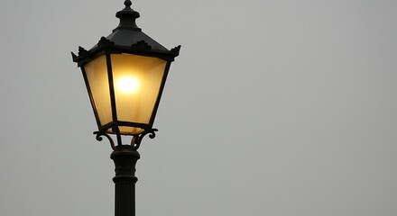 Vintage street lamp illuminates against a gray sky background