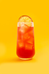 Red cocktail in a glass on a yellow background.