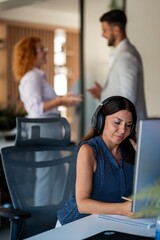 Focused businesswoman with headphones working while colleagues converse in modern office