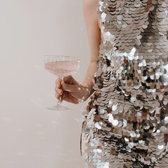 Beautiful woman wearing sparkling shining evening dress holding glass of pink champagne wine. Christmas, New Year holidays party event celebration. Cheers concept