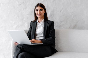 Smiling confident businesswoman working on laptop wearing casual formal wear, looking at camera