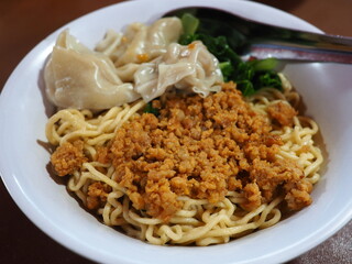 A bowl of noodles topped with vegetables and minced pork in soy sauce served with boiled dumplings.
