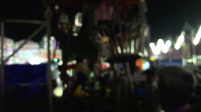 Colorful blurred night shot of a big lighted Ferris wheel in an Indian funfair park, with an abstract blurred background of people gathering and shopping at the local city night market