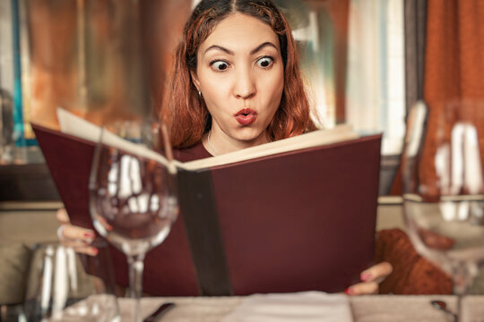 Woman expressing surprise and shock, eyes wide and mouth pursed, while looking at a menu in a restaurant