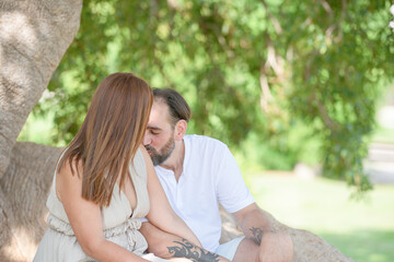 A man and a woman are sitting on a tree branch, kissing each other. Scene is romantic and intimate