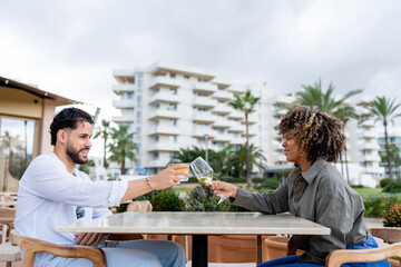 Diverse couple toasting drinks at outdoor cafe
