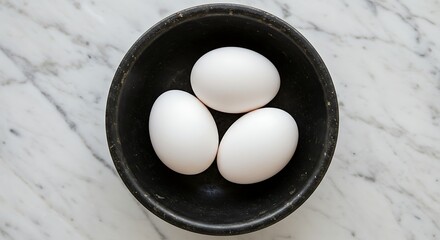 Three white eggs in a black bowl on a white marble surface