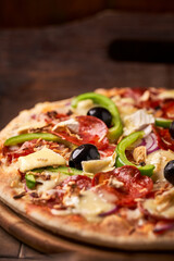Pizza with chorizo ​​sausage, mozzarella cheese, green pepper and black olives. Rustic wooden background. Soft focus.	