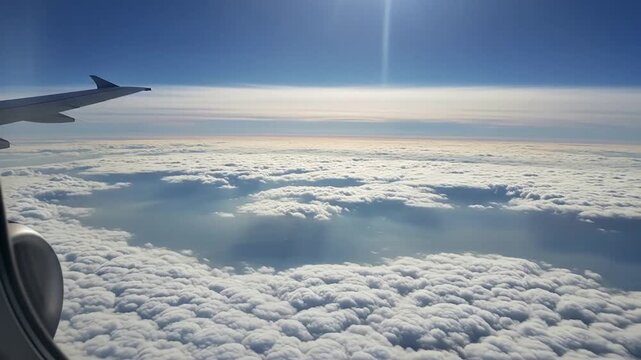 View from an airplane window, showcasing a vast expanse of clouds and the bright blue sky.