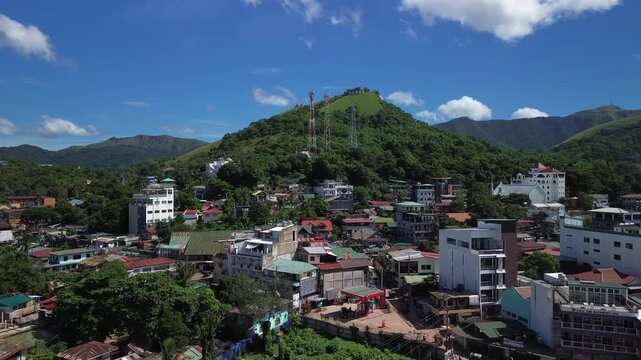 Aerial view over Coron town rooftops below Mount Tapyas with hilltop towers green slopes and bright blue sky on Busuanga Island Palawan
