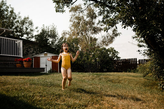 Young Girl Running Through Sprinkler in Summer in Backyard