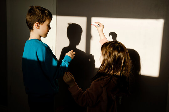 Siblings Playing with Light and Shadow Indoors