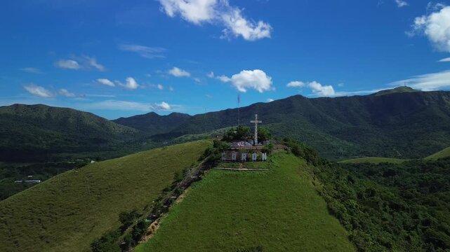 Close aerial view of Mount Tapyas summit above Coron with the hilltop cross large Coron letters green ridges surrounding mountains and clear daylight sky