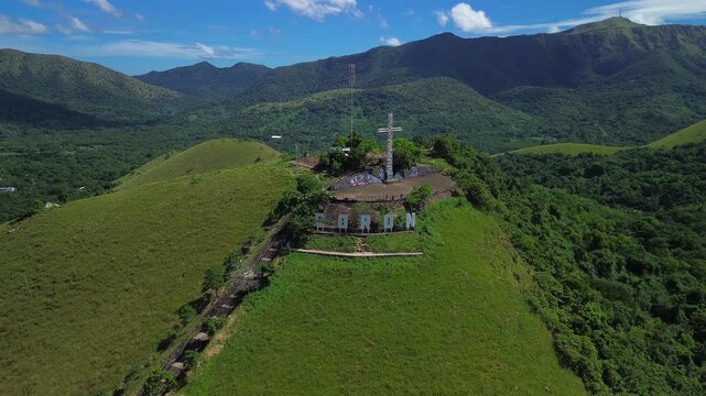 Aerial view of the Mount Tapyas hilltop cross and Coron letters on a green summit above forested valleys rolling ridges and bright daylight mountain scenery
