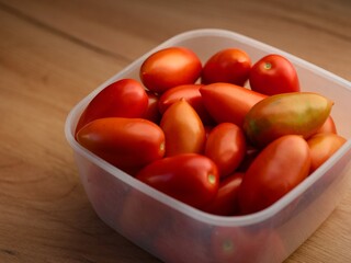 Plastic container full of red tomatoes on a wooden background