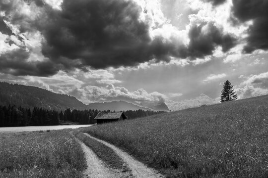 Black and white alpine landscape at Geroldsee with winding path, meadow and dramatic clouds